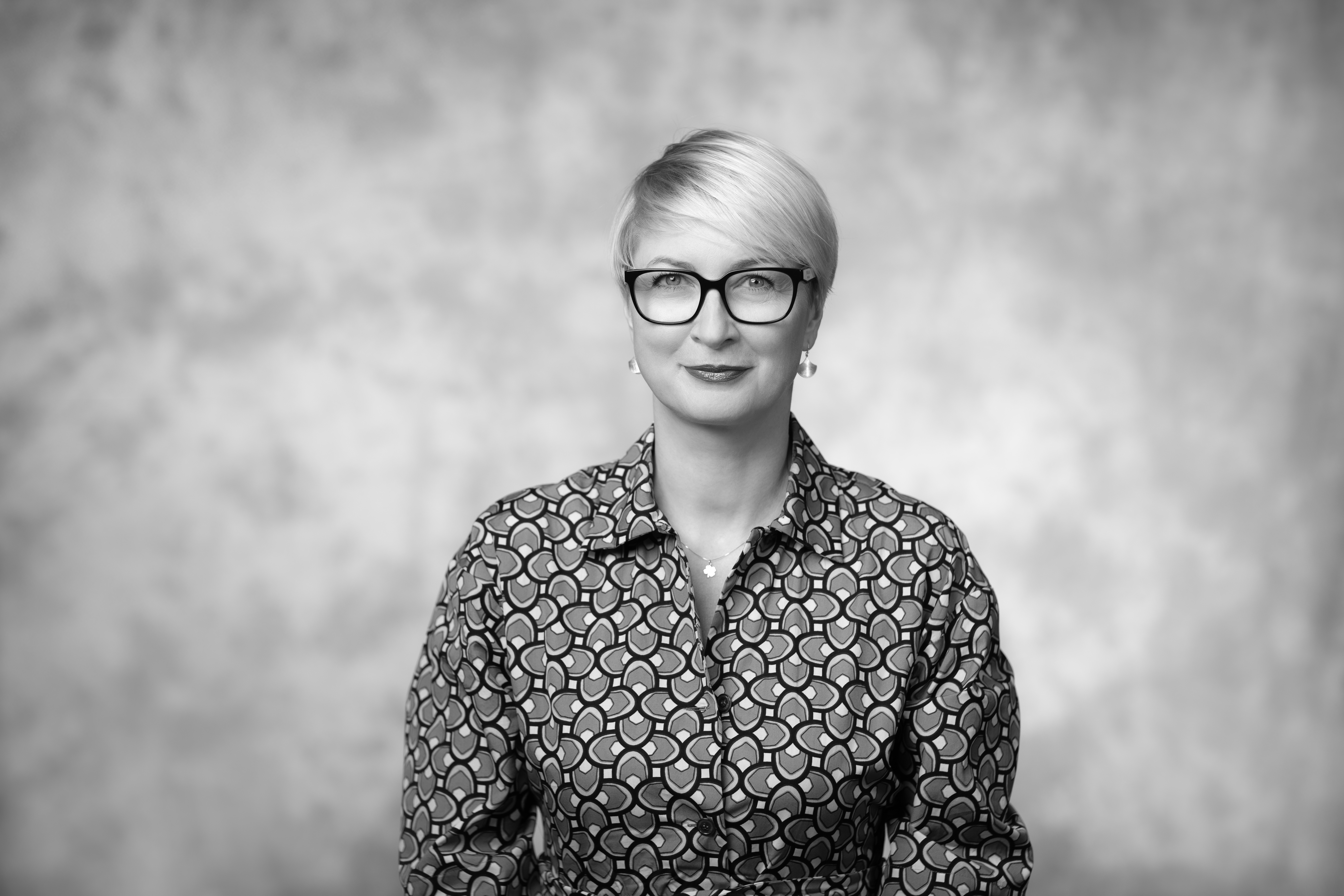 porter uśmiechniętej kobiety z krótkimi blon włosamia na szarym tle, foto czarno-białe