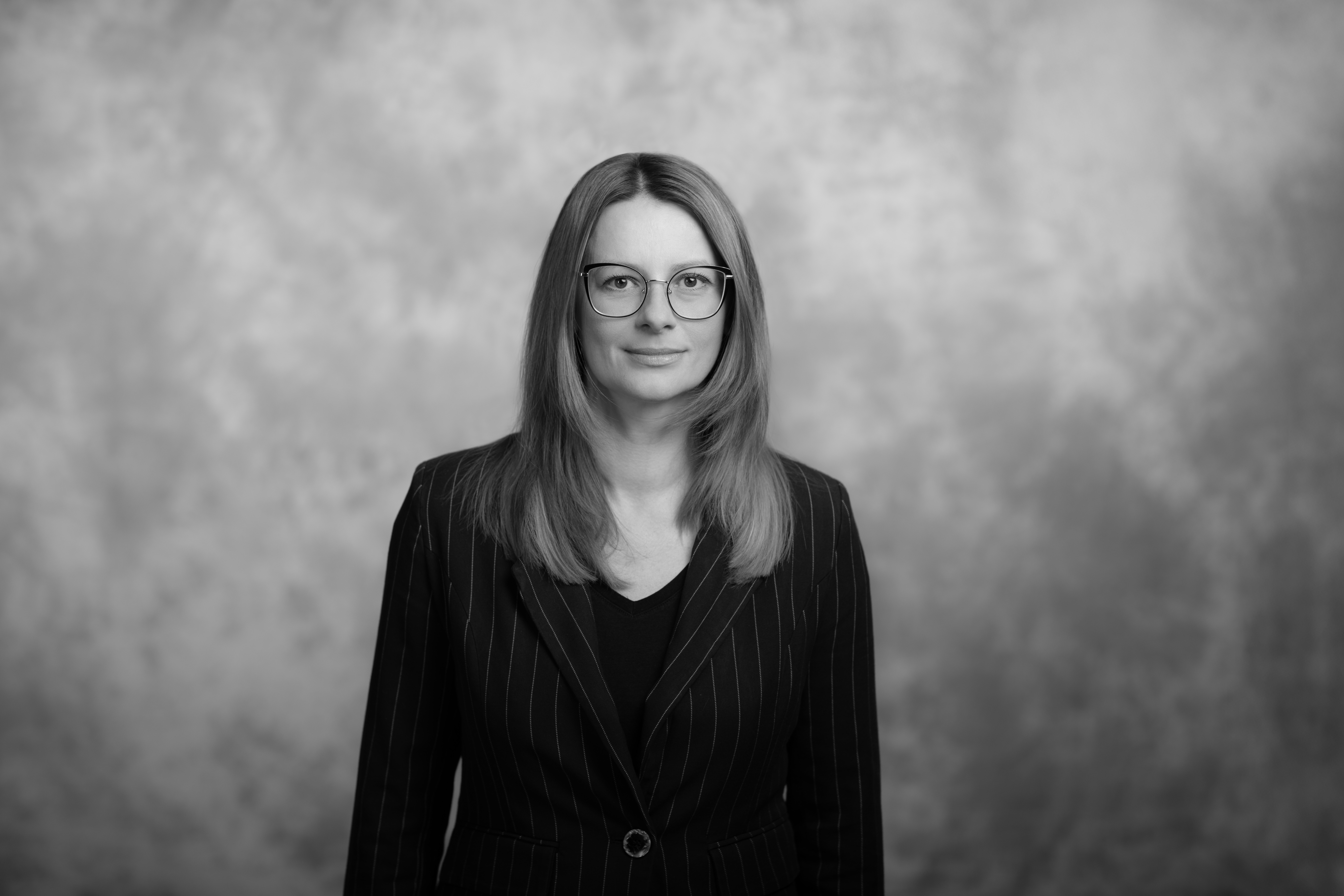 czarno-białę zdjęcie młodej kobiety w okularach na tle szarek ściany