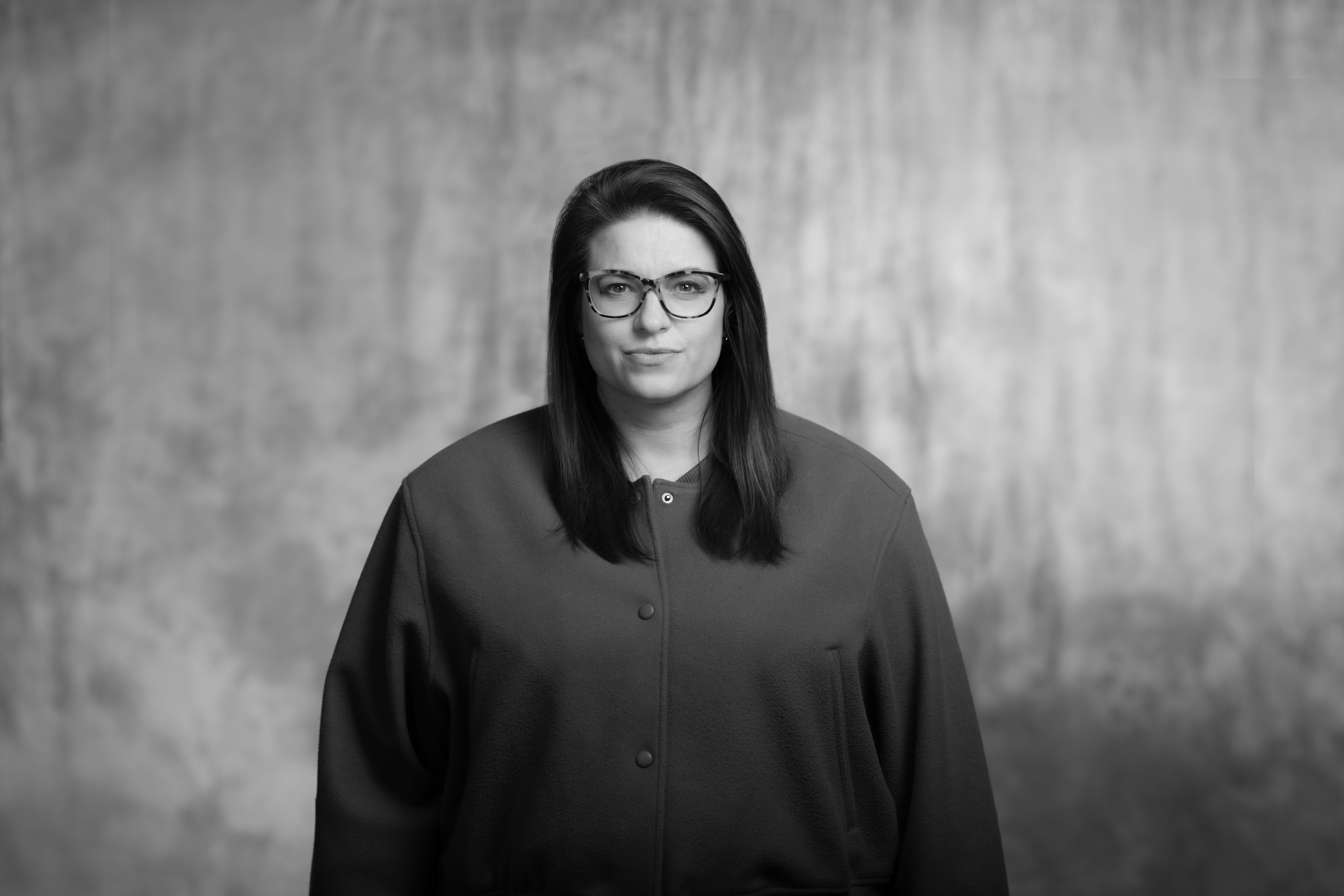 miczarno-biały portret kobiety w młodym wieku, rozpuszczone włosy i delikatny uśmiech, okulary z czarnymi oprawkac