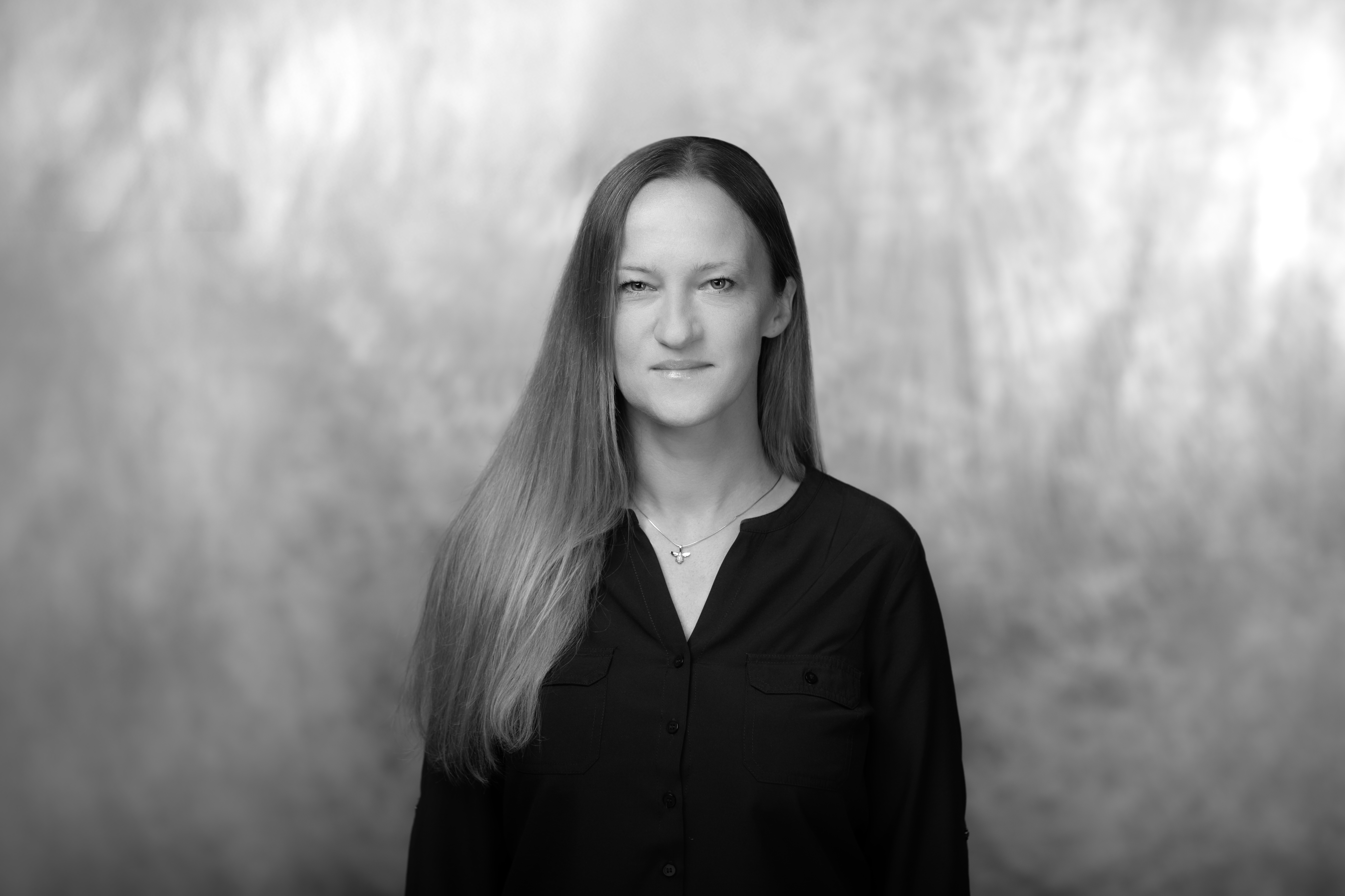 czafrno biały portret kobiety dojrzałej, uśmiechniętej, w czarnej kurtce i z kręconymi włosami długości do ucha