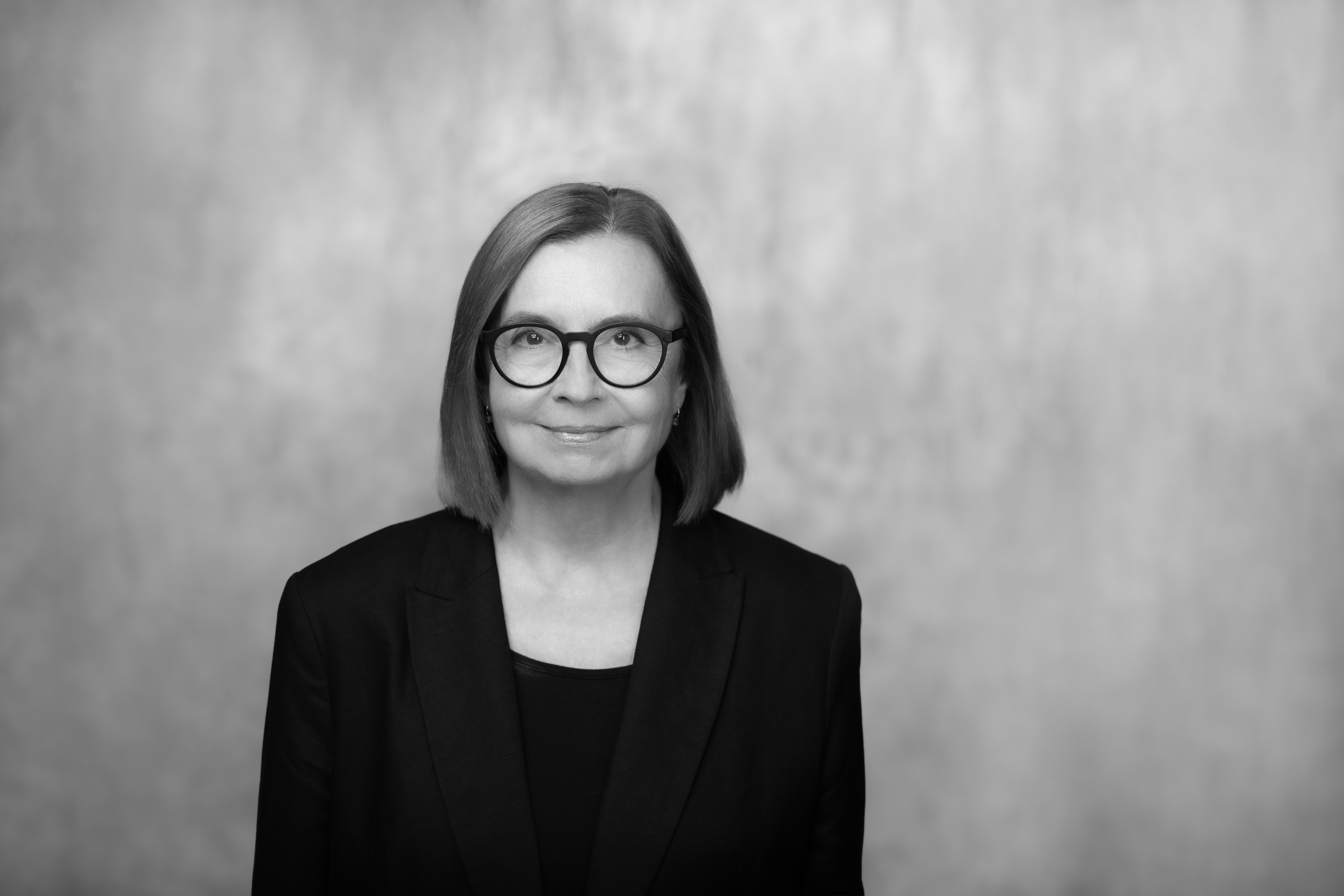 czarno-biały portret kobiety w dojrzałym wieku, rozpuszczone włosy i delikatny uśmiech, ma okulary w czarnych oprawkach