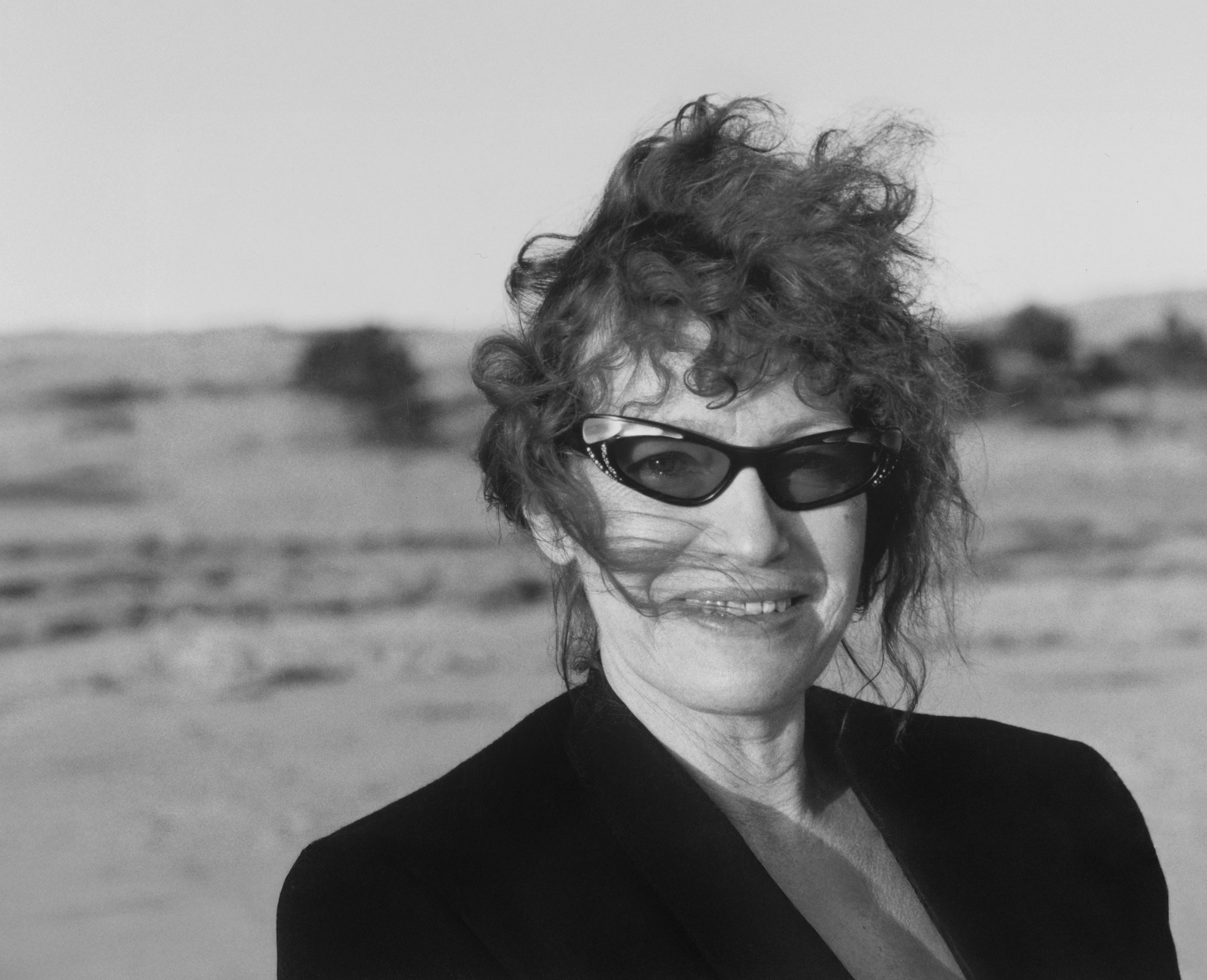 plenerowy portret kobiety w dojrzałym wieku, w okularach przeciwsłonecznych, z rozwianymi włosami