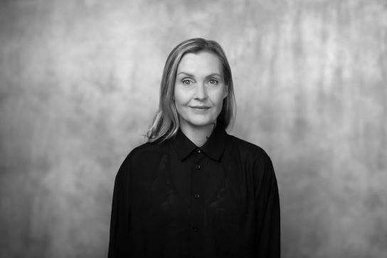 czafrno biały portret kobiety dojrzałej, uśmiechniętej, w czarnej kurtce i z kręconymi włosami długości do ucha