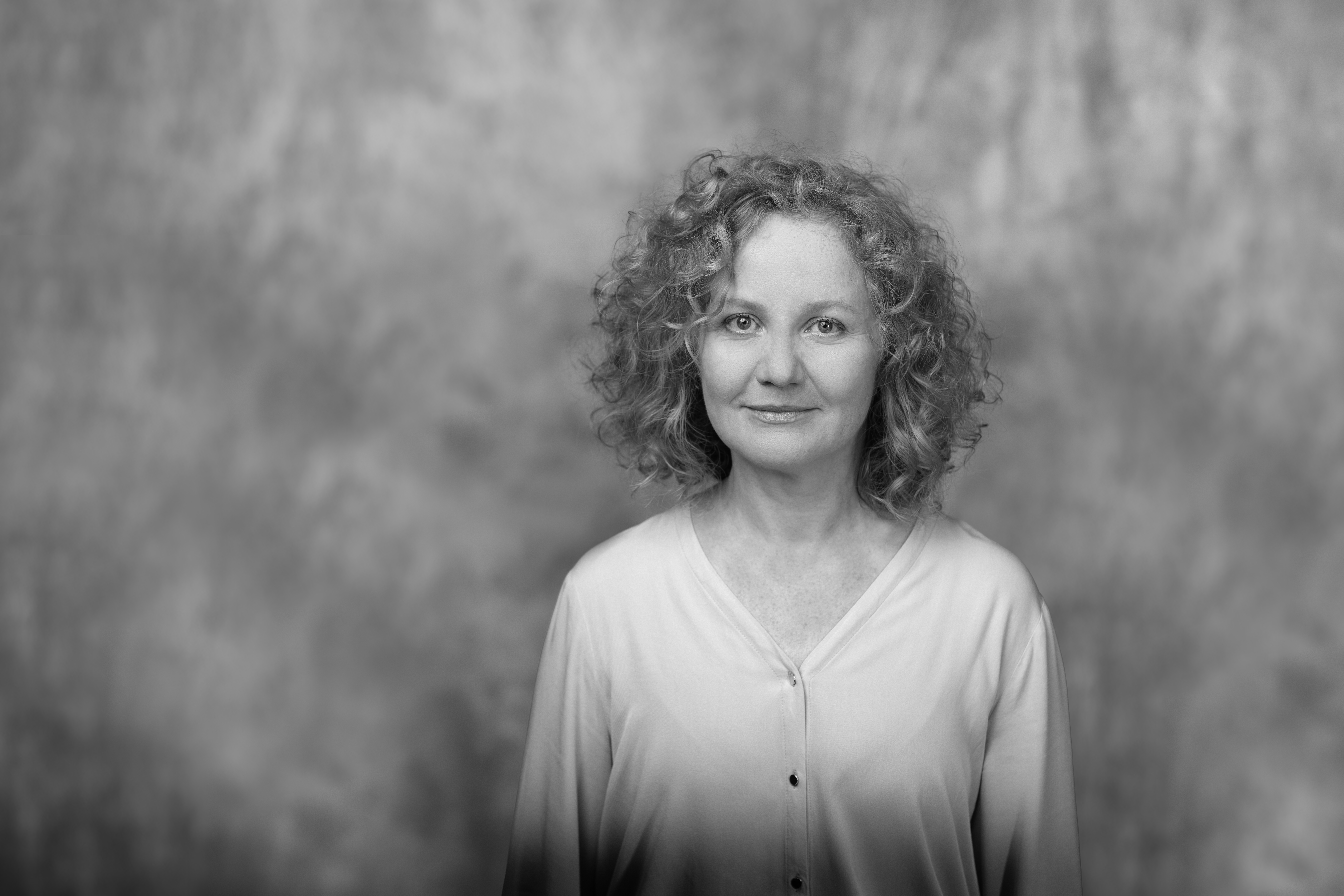 czarno-biały portret kobiety w dojrzałym wieku, rozpuszczone kręcone jasne włosy i delikatny uśmiech